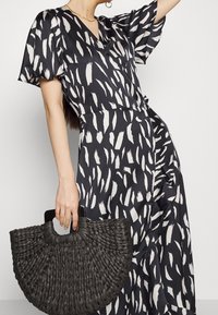 Robe à manches courtes en noir et blanc avec un motif de coups de pinceau. Un sac panier tissé noir texturé complète la tenue.
