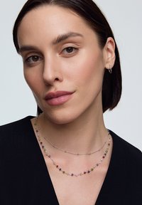 Naszyjnik z wielokolorowymi kamieniami szlachetnymi, składający się z małych, okrągłych koralików na srebrnym łańcuszku, warstwowy z delikatnym srebrnym łańcuszkiem. Gładka tekstura.