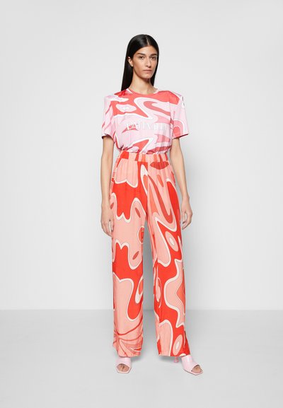 T-shirt rosa de manga curta com espirais vermelhas abstratas e logótipo, combinada com calças largas nas mesmas cores e sandálias de salto rosa claro.