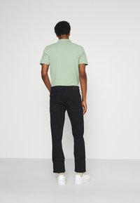 Camisa polo verde, jeans negros y zapatillas blancas. La polo tiene cuello y mangas cortas, los jeans tienen un corte estándar y bolsillos traseros.