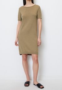 Knit short-sleeve dress in olive green, featuring a round neckline and straight cut. Worn with black slide sandals.