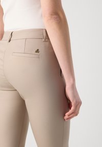 Beige skreddersydde bukser med en smal silhuett, med en liten gulllogo på baklommen og et glatt, teksturert stoff.