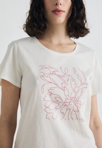T-shirt bianco in cotone con un disegno floreale a linee rosa, scollo rotondo, maniche corte e texture morbida. Design semplice e moderno.