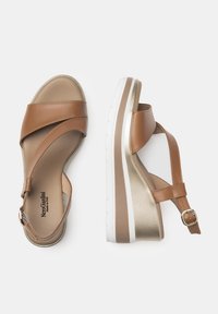 Sandali wedge in pelle marrone con cinturini incrociati, un accento dorato sul tallone e una suola a righe bianche. Si regolano con una chiusura a fibbia.