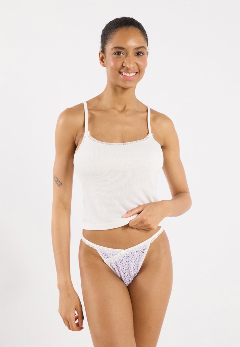 White ribbed tank top with thin straps, paired with floral lace trim thong featuring a purple and green pattern against a white background.