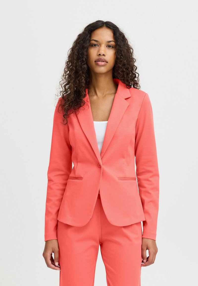Korallenfarbener Blazer mit slim fit, einreihiger Knopfleiste, Reverskragen und zwei Fronttaschen. Hergestellt aus glattem, strukturiertem Stoff.