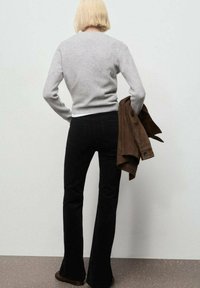 Suéter de lana gris, jeans acampanados negros, sosteniendo una chaqueta de ante marrón. Textura suave, diseño simple y colores neutros.