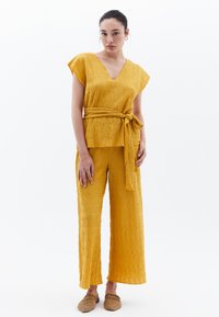 Un ensemble à deux pièces texturé jaune comprenant un haut à col en V avec des manches courtes et une taille nouée, associé à un pantalon large et décontracté.