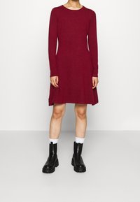 Burgundy pitkähihaineen mekko, joka on valmistettu pehmeästä kankaasta, pyöreällä pääntiellä ja levenevällä helmalla. Yhdistetty mustiin paksupohjaisiin nilkkabootseihin ja valkoisiin sukkiin.