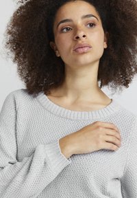 Helles graues, gestricktes Sweatshirt mit einem weiten, gerippten Halsausschnitt und gerippten Bündchen. Besitzt eine strukturierte Oberfläche und eine lässige Passform.