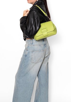 Donna che indossa jeans azzurri a gamba larga e giacca di pelle nera, con una borsa verde lime a tracolla.