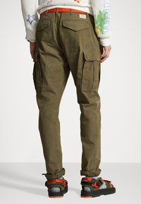 Olivgrön cargobyxor med en avsmalnande passform, med cargofickor och ett kontrasterande orange bälte. Strukturerad bomullstyg med en hållbar känsla.