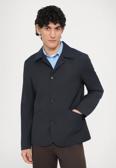 Tengerészkék egysoros zakó notches gallérral, három gombbal és oldalzsebekkel, strukturált szövetből készült.