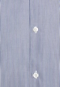 Gestreept shirt in wit en marineblauw, gemaakt van katoen, met verticale lijnen, een kraag en een witte knoop in het midden aan de voorkant.