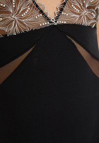 Robe noire avec superposition en mesh transparent ornée de broderies florales. Le design croisé au niveau du col ajoute de la texture et de l'intérêt visuel.