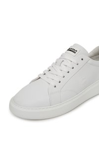 Balts ādas sporta apavu arapaļš purngals, plakanu baltu zoli, tonālām šuvēm un mežģīnēm. Uz mēles ir redzama logotipa uzlīme.