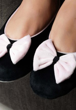 Chaussures plates noires avec des nœuds en velours rose sur les orteils. Texture douce en daim, forme arrondie et semelle plate. Vue en gros plan de la chaussure.