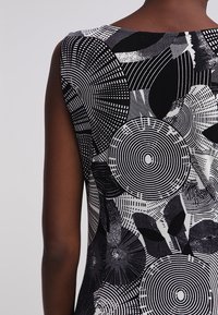 Ärmlös svart och vit klänning med abstrakta cirkulära och linjära mönster, bärs av en person med mörk hud, sedd bakifrån.