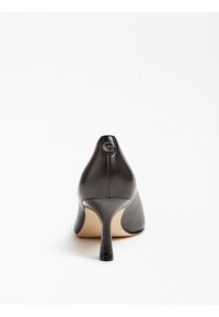 Escarpins en cuir noir à talons aiguilles avec un bout pointu, présentant un design élégant et un petit détail de logo métallique à l'arrière.