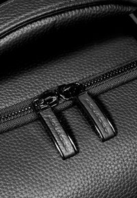 Mochila de cuero negro con superficie texturizada, que cuenta con un cierre doble de cremallera negra y etiquetas de tirador de cremallera en relieve.