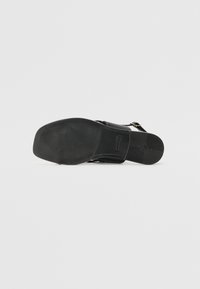 Sandalie negre cu o talpă din cauciuc texturat, curea de gleznă ajustabilă și accente metalice. Prezintă un superior din piele netedă și un design minimalist.