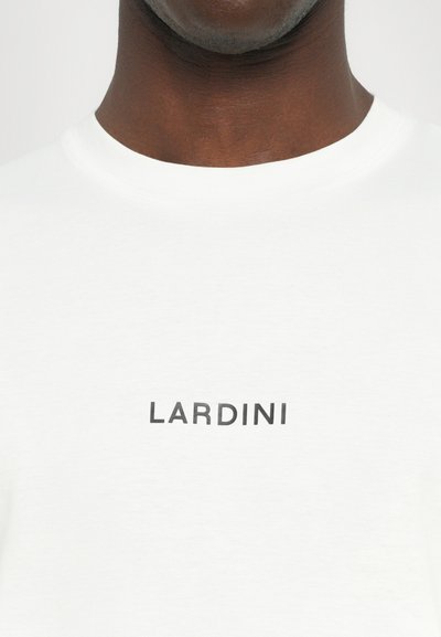Valkoinen puuvillapaita, jossa on pyöreä kaula-aukko ja painettu musta logo, jossa lukee "LARDINI" rinnan kohdalla. Pehmeä, sileä pinta.