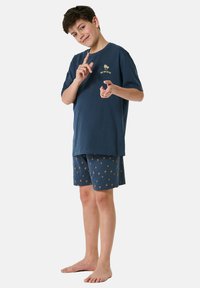 Navy cotton t-shirt with gold palm tree logo paired with navy shorts featuring a yellow palm-pattern design. Casual, lightweight outfit.