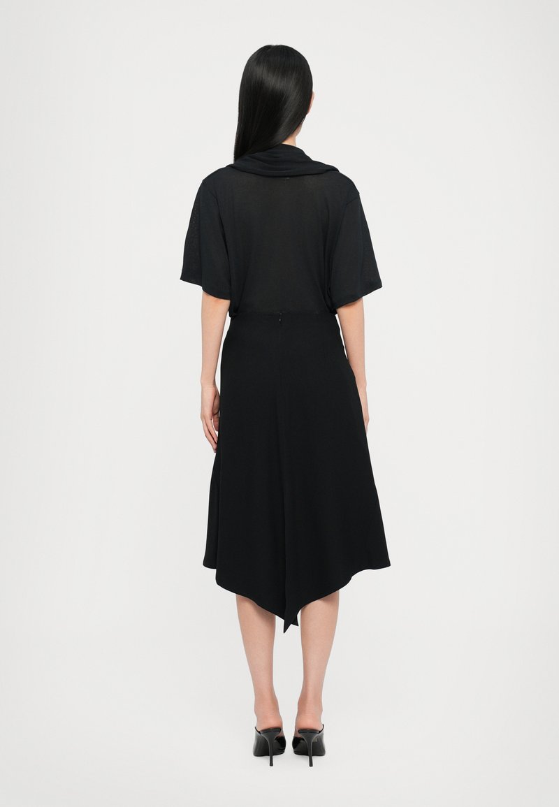 Black dress with short sleeves, flowing silhouette, curved hemline, and smooth texture. Paired with black high-heeled shoes.