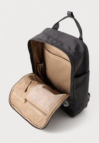 Black fabric backpack with a tan interior, featuring a zippered mesh pocket, elastic organizer, and a top handle for easy carrying.