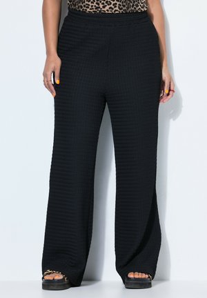 Osoba nosząca czarne szerokie spodnie o fakturze, top w panterkę, sandały na platformie w panterkę oraz pomarańczowy lakier na paznokciach dłoni i stóp.