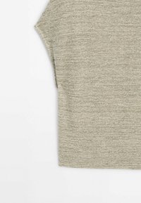 Tissu tricoté gris clair avec un motif côtelé texturé et un détail de manche pliée sur fond blanc uni.