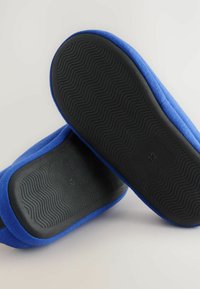 Blå stofslip-ons med en sort gummiydersål. Tekstureret sål for optimal greb, med en størrelsesmærkat "12" på bunden. Enkel design.
