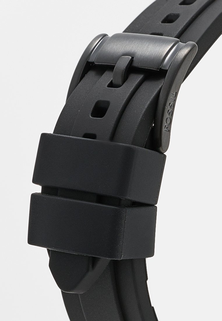 Schwarzes Silikon-Uhrenarmband mit strukturiertem Oberflächen, mehreren verstellbaren Löchern und einer matte schwarzen Schnalle mit geprägt Logo-Detail.