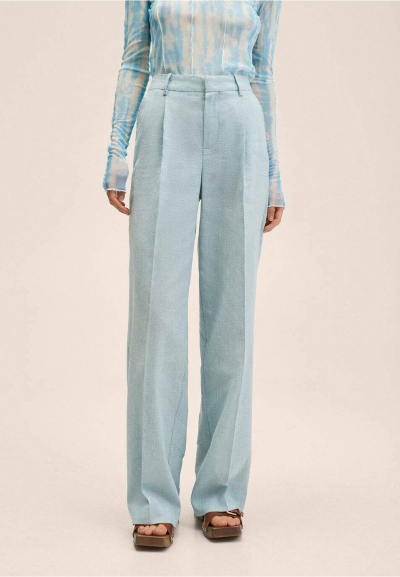 Femme portant un pantalon taille haute bleu clair à jambes larges, un haut à manches longues bleu et blanc à motifs, et des sandales marron avec des nœuds.