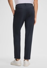 Granatowe spodnie z tkanym wzorem, elastycznym paskiem w talii i dwiema tylnymi kieszeniami. W połączeniu z jasnoszarymi sneakersami.