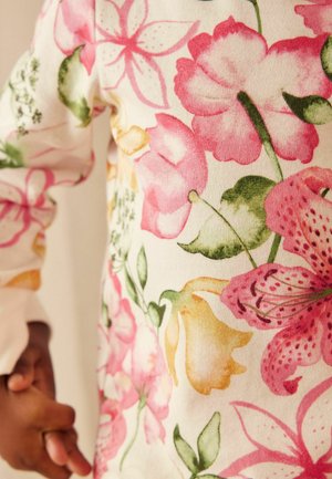 Tejido de algodón con estampado floral que presenta flores en tonos rosa, amarillo y verde sobre un fondo crema, con una textura suave y colores vibrantes.