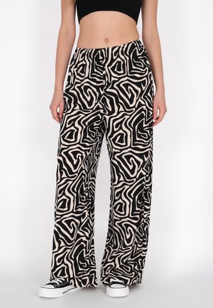 Kvinde iført sorte og hvide bukser med abstrakt mønster, sort crop top og sorte og hvide sneakers.