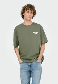Olijfgroen t-shirt met korte mouwen en het "Solo Rider" logo in het wit. Comfortabele fit met een ronde halslijn. Draag het met lichtblauwe spijkerbroek.