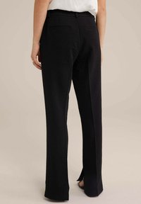 Črne hlače z teksturirano tkanino, slim fit kroja in zadnjimi žepi. Imajo stranske razpoke na robu. Kombinirane so z belim topom in črnimi sandalami.