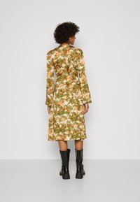 Robe midi à motifs floraux en vert, orange et blanc ; présente des manches longues, une taille cintrée et une jupe fluide. Portée avec des bottes noires jusqu'aux genoux.