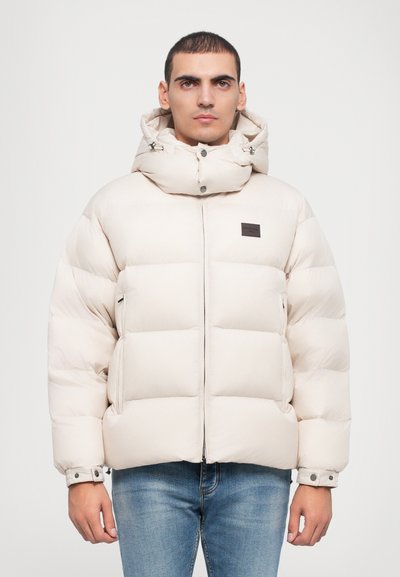 Giubbotto imbottito color beige chiaro, con colletto alto, chiusura zip frontale e tasche laterali; realizzato con pannelli trapuntati per l'isolamento.