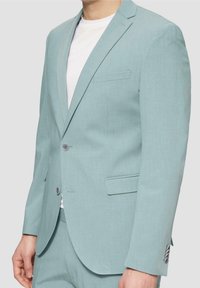 Lichtblauw colbert gemaakt van gestructureerde stof. Voorzien van een enkele knoopsluiting, notched revers en een borstzak. Draagt over een wit overhemd.