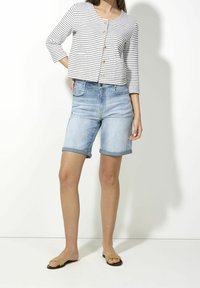 Raitapuintopaita, jossa on nappikiinnitys, yhdistettynä vaaleansinisiiin denim-bermudashortseihin. Saappaat ovat yksinkertaisella tasapohjalla.
