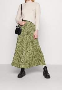 Maglione beige lavorato a maglia con vestibilità ampia, abbinato a una gonna maxi verde con stampa floreale. Il look è completato da una borsa nera e stivali con plateau.