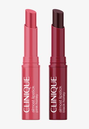 Deux tubes de rouge à lèvres Clinique Almost, l'un en teinte pink honey et l'autre en teinte black honey, avec le rouge à lèvres partiellement sorti.
