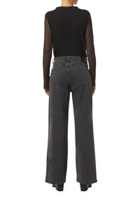 Schwarzes langärmeliges Oberteil mit gerippter Textur und transparenten Ärmeln, kombiniert mit hochtaillierten, weit geschnittenen grauen Jeans aus Denim mit Taschen auf der Rückseite.