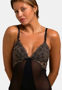 Body en dentelle noire avec des motifs floraux, décolleté plongeant, bretelles ajustables et maille transparente dans la partie inférieure.