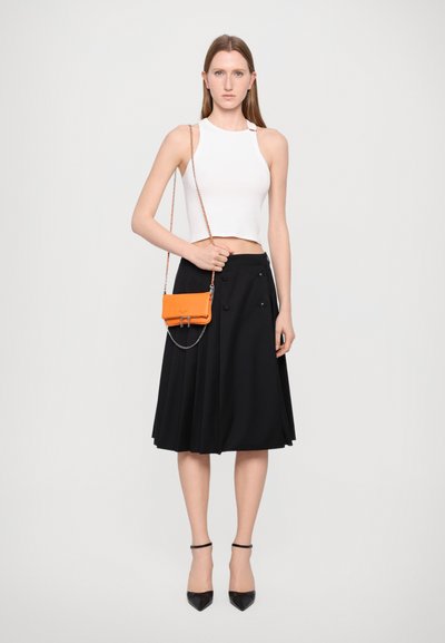 Top cropped bianco, gonna nera a pieghe e borsa a tracolla arancione con catena. Tacchi a punta neri completano l'outfit.