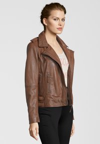 Braune Leder-Motorradjacke mit breiten Revers, asymmetrischem Reißverschluss und mehreren Reißverschlusstaschen. Getragen über einem hellen Hemd.