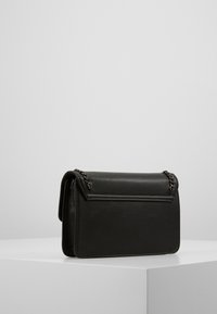 Bolso de hombro de imitación de cuero negro con un detalle de cadena, forma rectangular, textura suave y cierre de solapa. Diseño minimalista sin patrones.